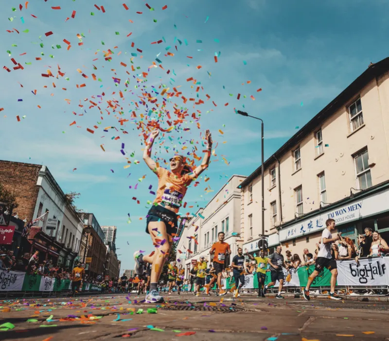 Woman running through colourful paper ribbons